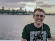 Me smiling at the camera at golden hour, a river and the Quebec City skyline behind me, a camera strap over one shoulder.